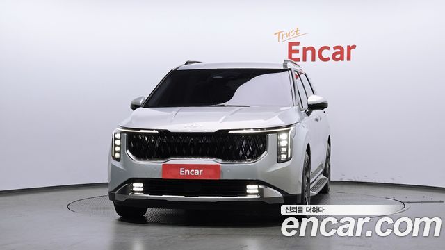 Крупный план передней части Kia Carnival HEV 2024, видна чёрная решётка радиатора, дневные ходовые огни и эмблема Kia.
