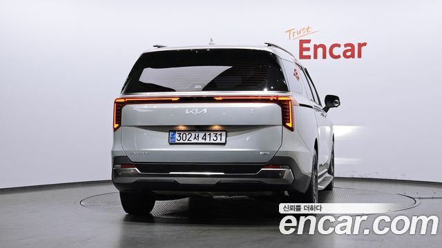 Крупный вид сзади Kia Carnival 2024, заметна эмблема на багажнике, световая полоска и форм-фактор минивэна в салоне шоурума.