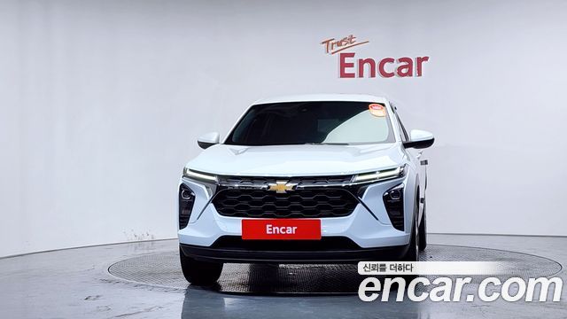 Фронтальный вид белого Chevrolet Trax 2024 в павильоне Encar; крупный план решётки радиатора, эмблемы Chevrolet и общего внешнего вида передней части.