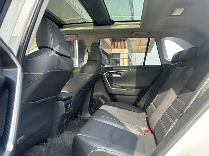 Салон Toyota RAV4: задний ряд сидений с чёрной обшивкой, подлокотник и панорамная крыша, пространство для пассажиров видно с правого ракурса.