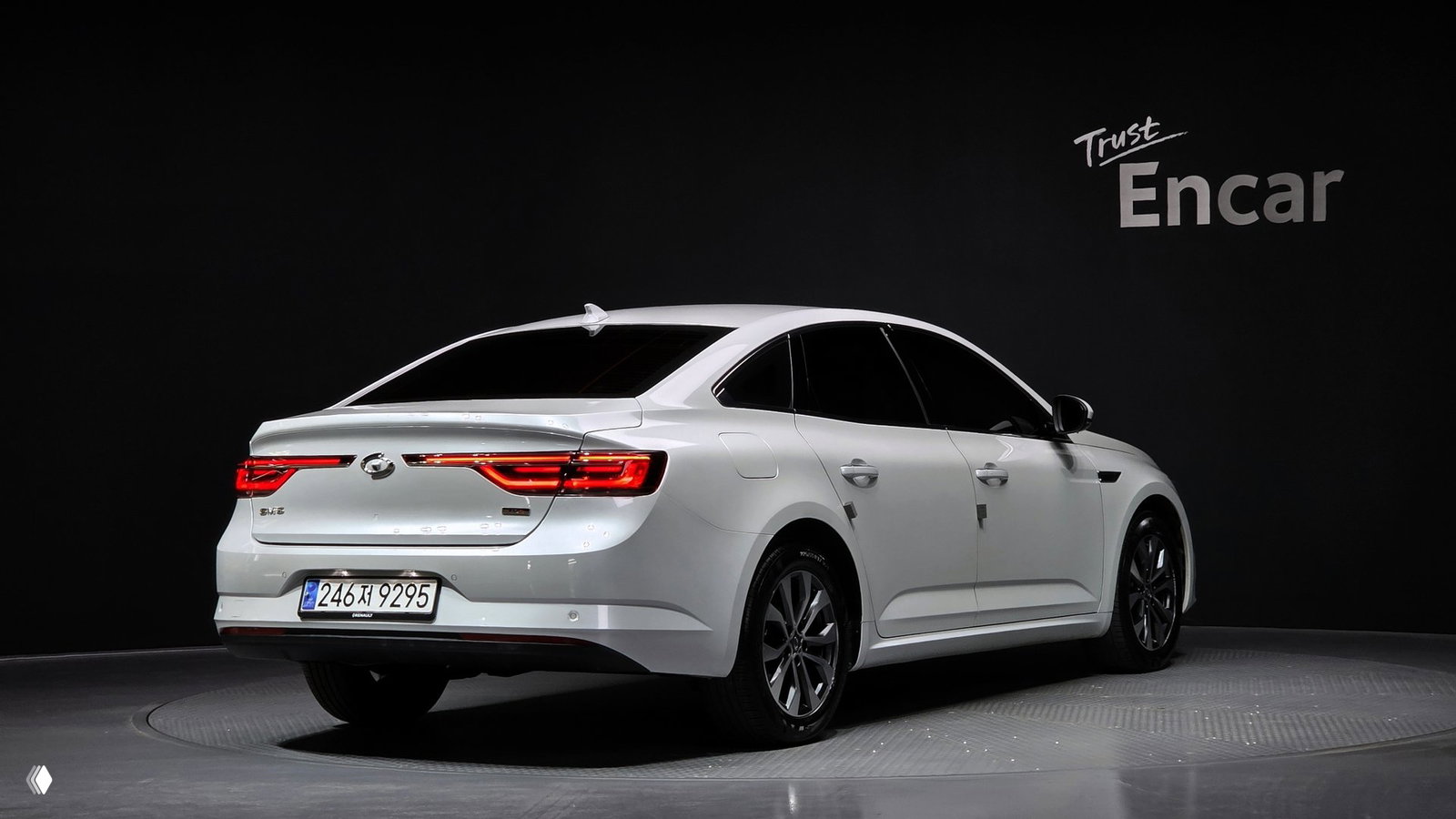 Задний трёхчетвёртной вид белого Renault Samsung SM6 на поворотном подиуме, видны задние фонари, спойлер и регистрационный номер, логотип Encar на стене.