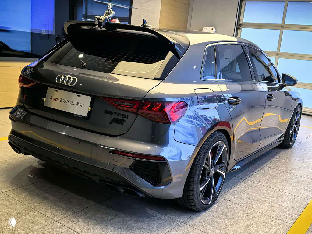 Задняя часть Audi A3 Sportback 2022 серого цвета в шоуруме: вид на багажник, задние фонари и спортивный диффузор внизу бампера.