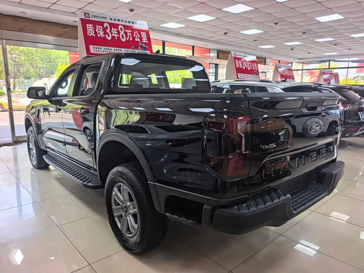 Задняя часть чёрного Ford Ranger в выставочном зале: кузов пикапа, задние фонари и отражение шоурума на лаке кузова.