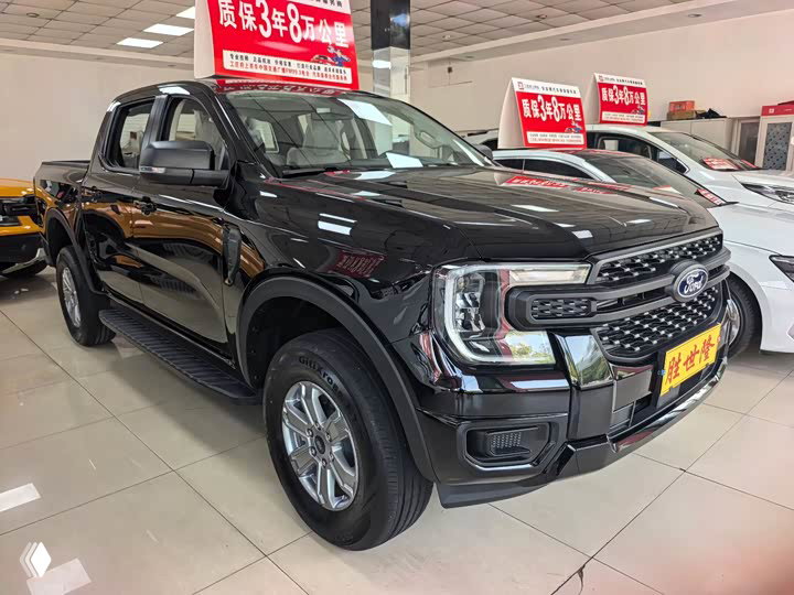 Фронтально-боковой ракурс чёрного Ford Ranger в салоне: решётка радиатора, фары, колёса и информационные таблички дилерского центра.