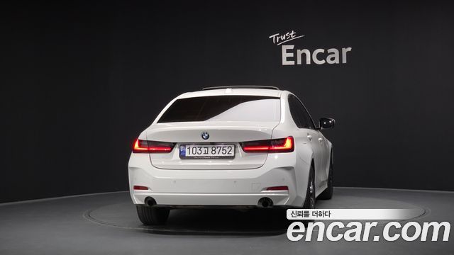 Белый BMW 3 Series 320i 2024 — вид сзади в выставочном зале Encar, видны задние фонари и номерная табличка.