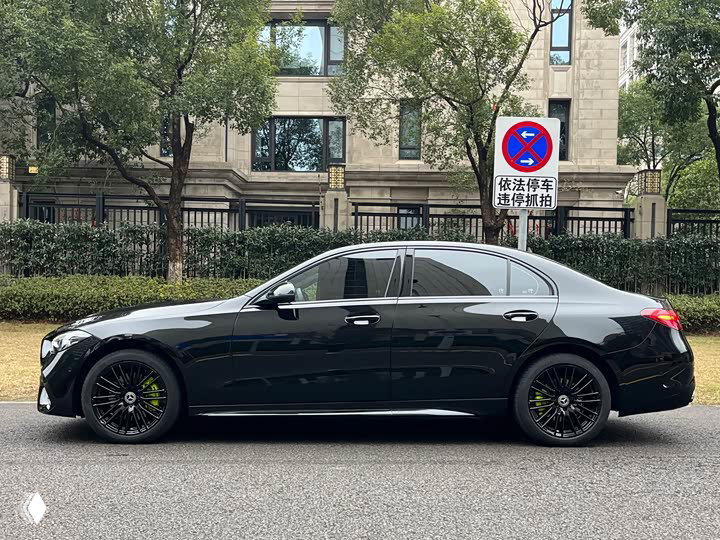 Боковой профиль черного Mercedes‑Benz C 260 L 2023 года, автомобиль в профиль на улице с зеленью и домами на заднем плане.