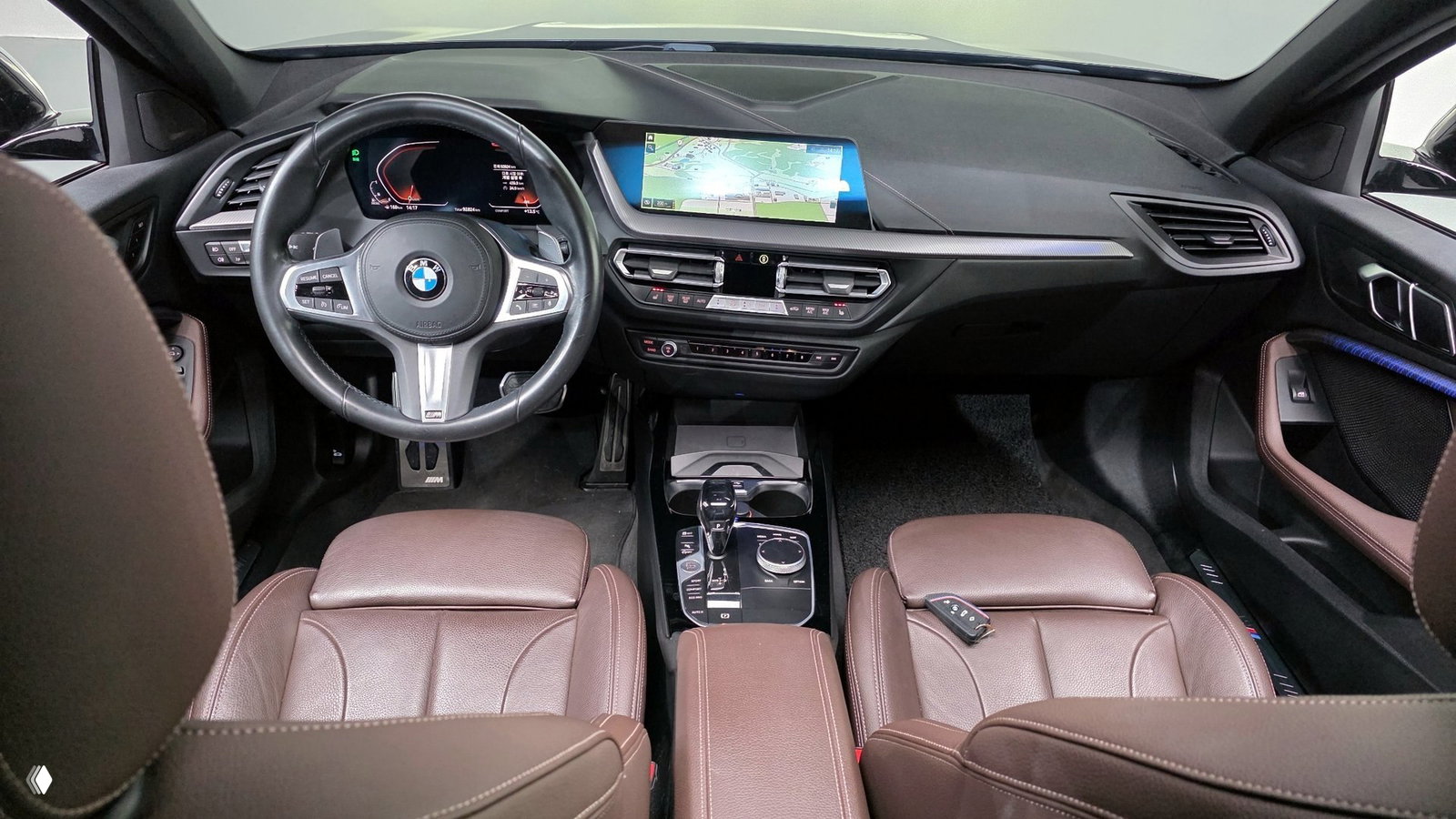 Интерьер BMW 1 Series F40: рулевое колесо M Sport, коричневые кожаные передние сиденья, центральная консоль с селектором коробки и экраном навигации.