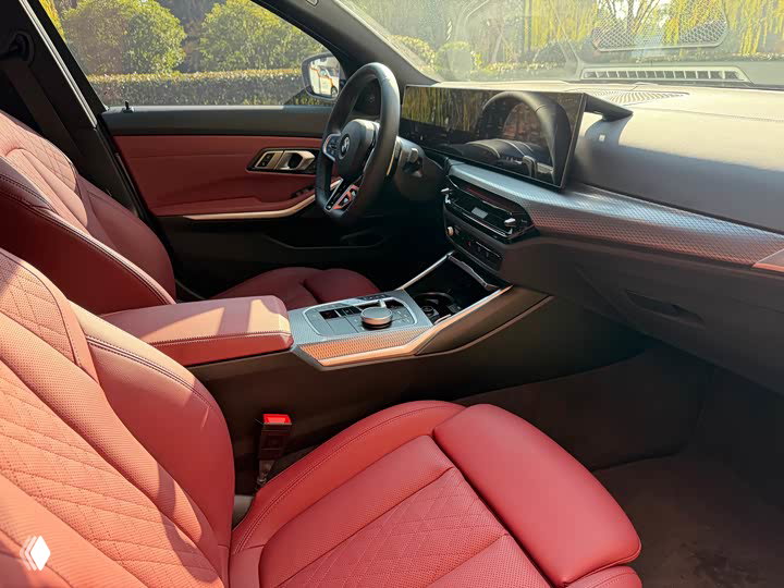Центральная консоль и передние красные кожаные сиденья BMW 3 330Li M 2025: джойстик управления, элементы отделки и рукоять переключения передач в кадре.