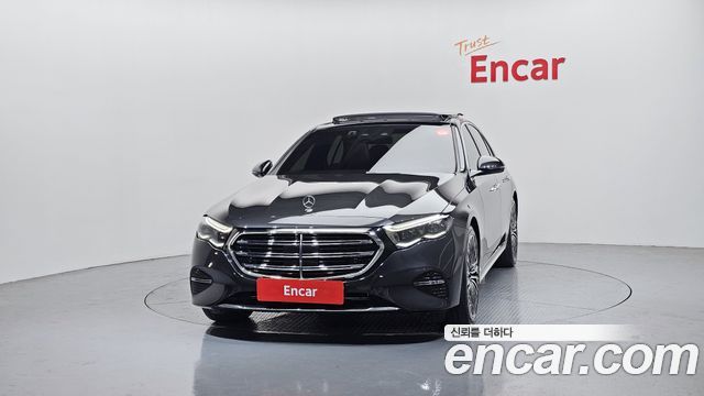 Фотография Mercedes-Benz E450 2024 анфас в дилерском павильоне, видна эмблема и передняя оптика на тёмно‑сером кузове