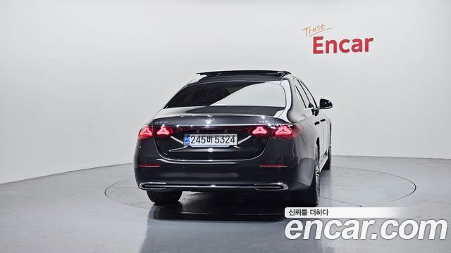 Фото Mercedes‑Benz E‑Class E450 2024 сзади на поворотном подиуме, виден корейский номер и логотип Encar на стене фона