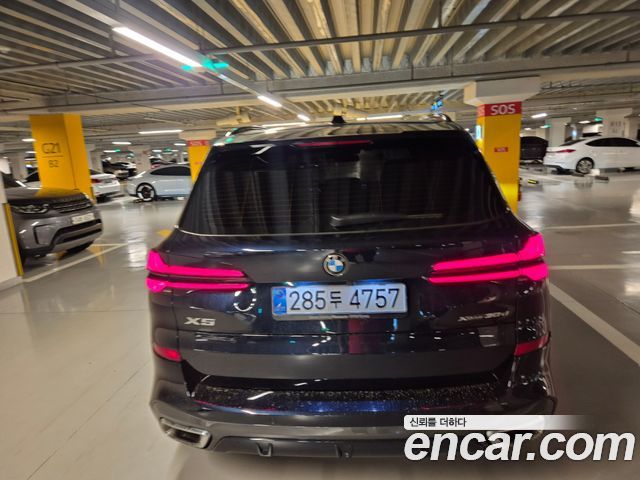 Крупный вид задней части BMW X5 xDrive 30d 2026 в паркинге; видны задние фонари, эмблема, детали бампера и выхлопные патрубки.