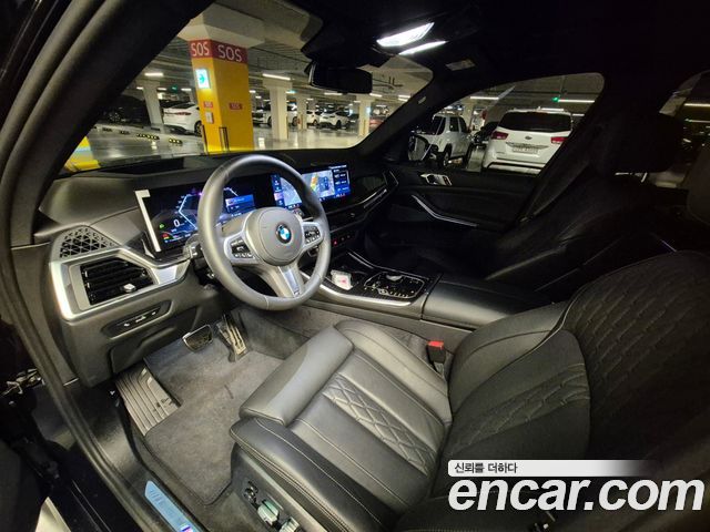 Интерьер BMW X5 xDrive 30d M Sport 2026: передняя панель, руль, цифровая приборная панель и мультимедийный экран, чёрная отделка сидений.