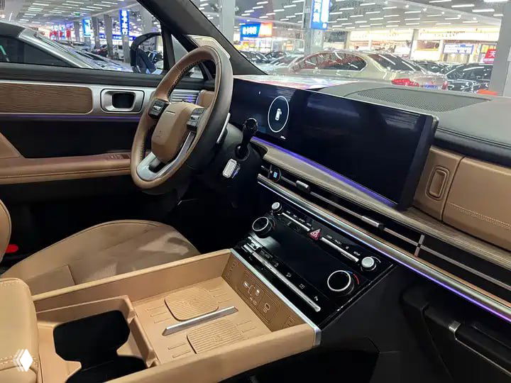 Интерьер Hyundai Santa Fe 2024: торпедо с широким сенсорным экраном, коричневый кожаный салон и рулевое колесо, снимок сделан в шоуруме.