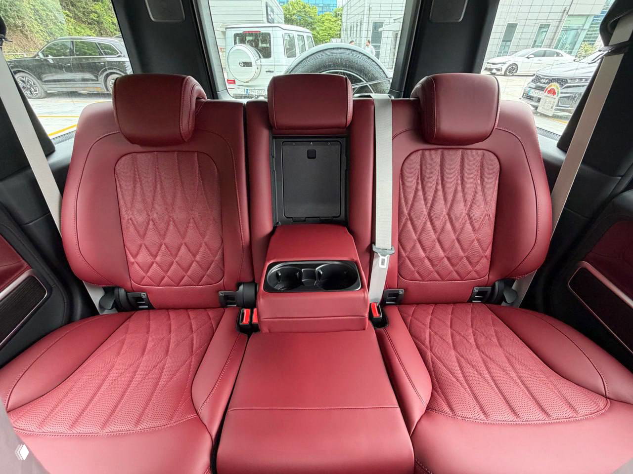 Задний ряд сидений Mercedes‑AMG G63 2026 в красной кожаной отделке с центральным подлокотником и чашками для напитков, фото салона для покупателей.