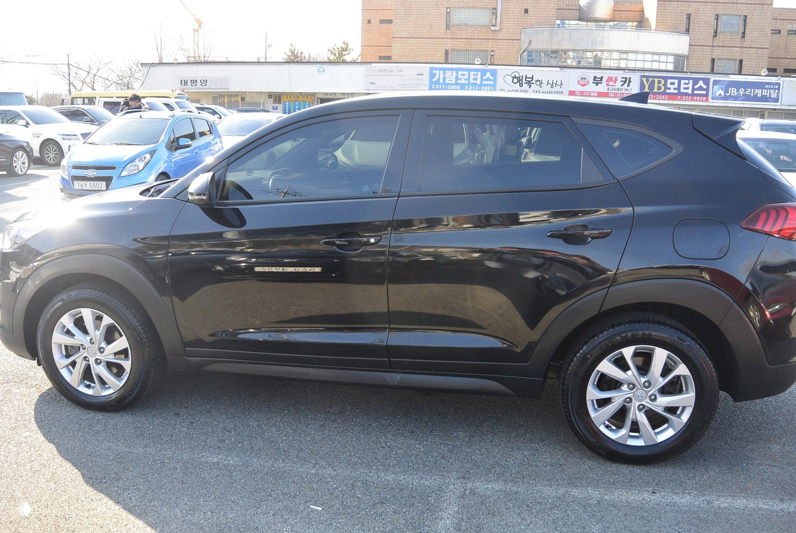 Черный Hyundai Tucson 2020, вид сбоку — профиль, колеса и дверные панели на парковочном пространстве автосалона.