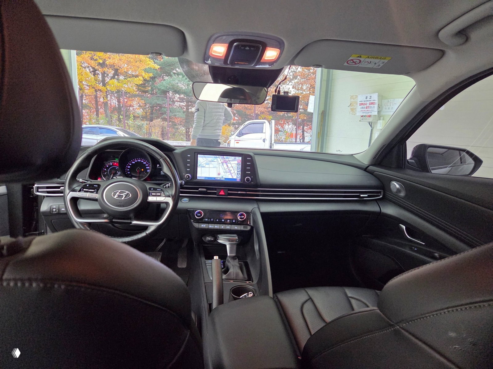 Интерьер Hyundai Avante: вид на руль с логотипом Hyundai, мультимедиа‑экран, центральная консоль и передние кожаные сиденья, салон в тёмных тонах.