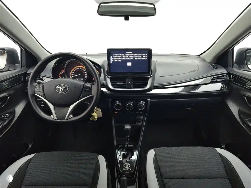 Интерьер Toyota YARiS L: приборная панель, рулевое колесо с логотипом Toyota, мультимедийный экран и центральная консоль с коробкой CVT.