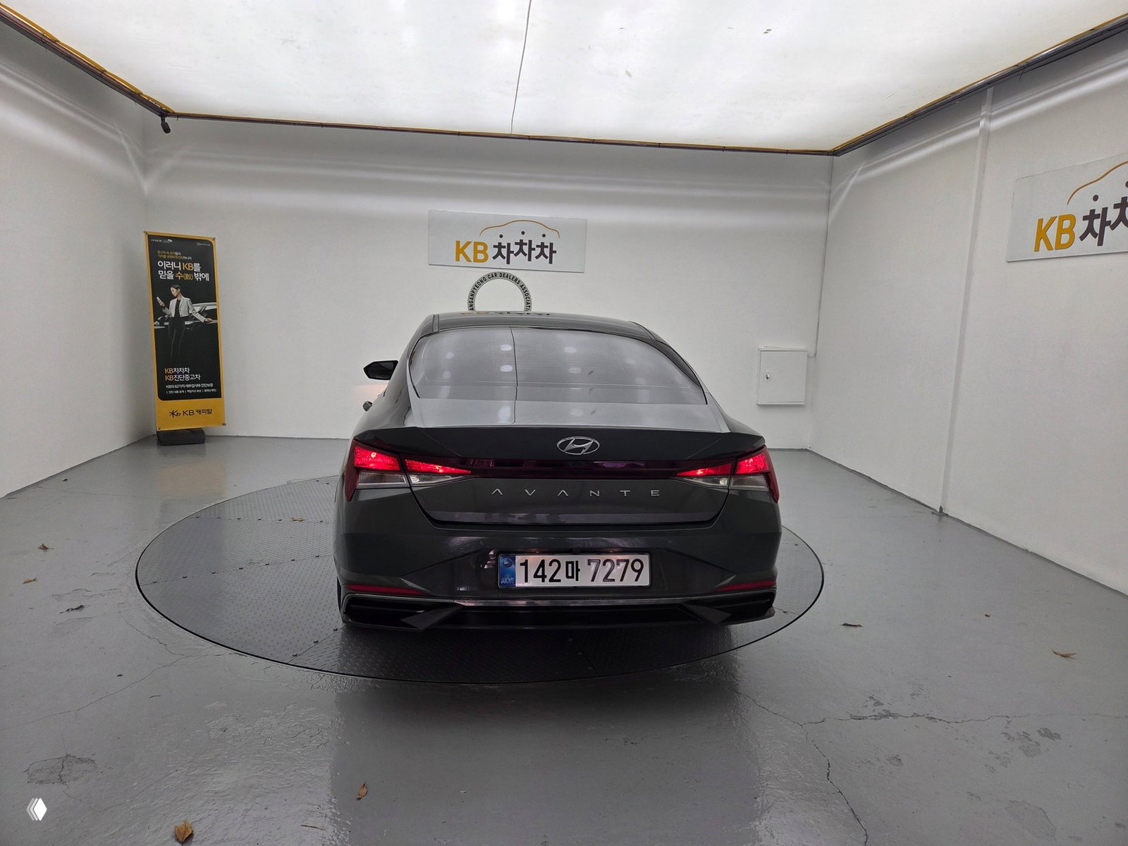 Задний вид Hyundai Avante CN7 2021: багажная крышка с надписью AVANTE, светодиодные фонари и корейский номер, автомобиль на вращающейся платформе в фотозоне дилера.