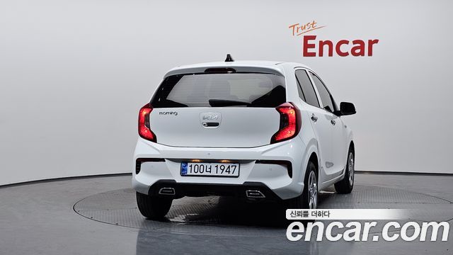 Ещё один ракурс задней части белого Kia Morning на вращающемся стенде Encar — акцент на кузове, бампер и состояние лакокрасочного покрытия.