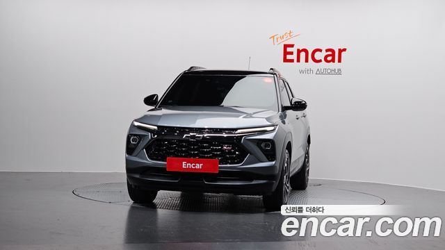 Фронтальный вид серого Chevrolet Trailblazer 2024 в шоуруме Encar, заметна решётка радиатора, детали фар и логотип продавца incar/encar.
