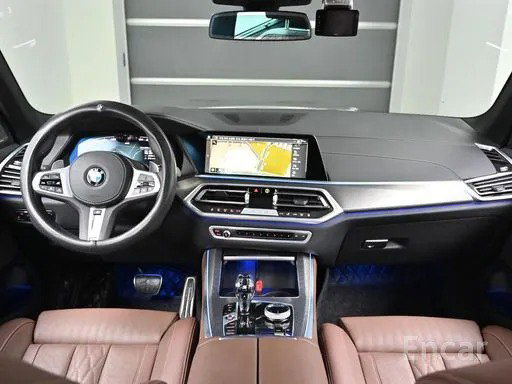 Салон BMW X5: ракурс приборной панели и центрального тоннеля с навигацией, кожаные сиденья и мягкая подсветка.