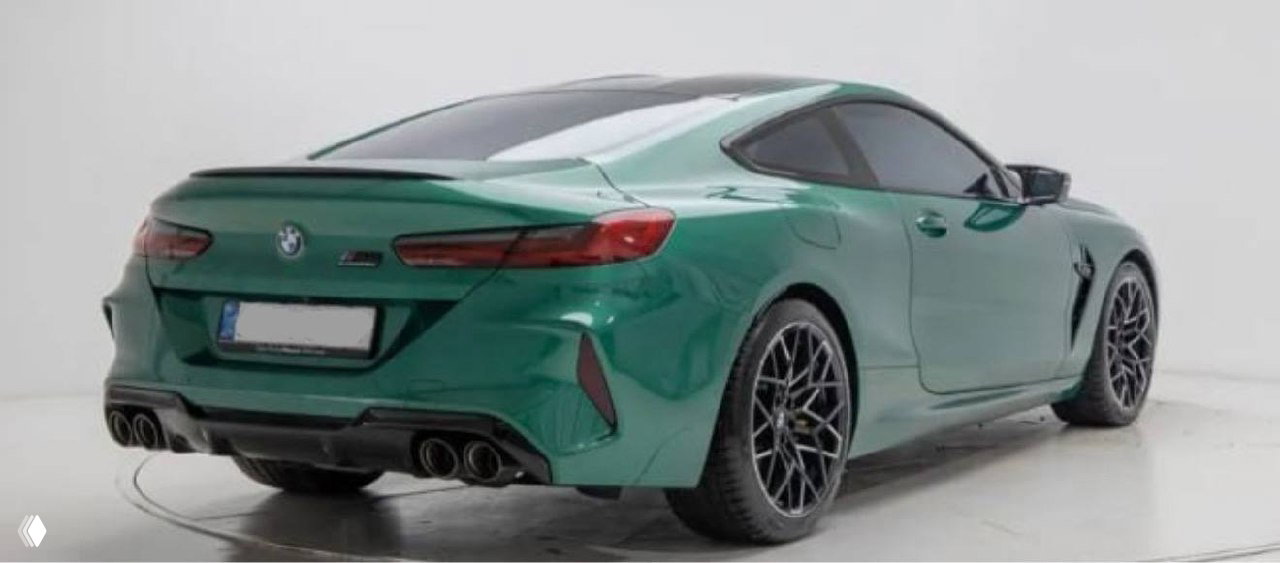 Задний трёхчетвертной вид зелёного BMW M8 Competition: заметны задние фонари, диффузор и четыре патрубка выхлопа на студийном фоне, демонстрация состояния кузова.