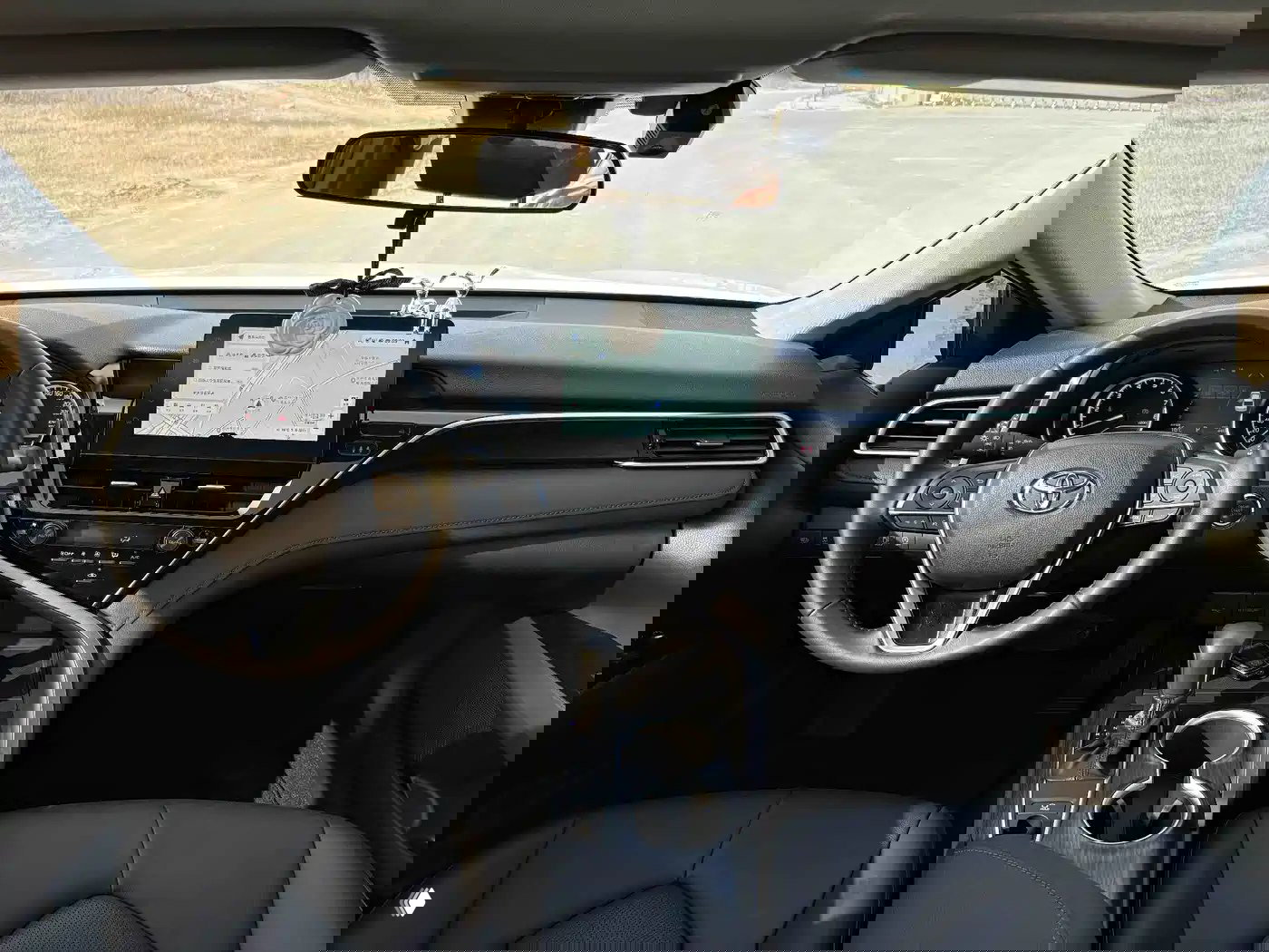 Интерьер Toyota Camry 2023: панорамный вид на руль, приборную панель, сенсорный экран навигации и центральную консоль с селектором коробки CVT.