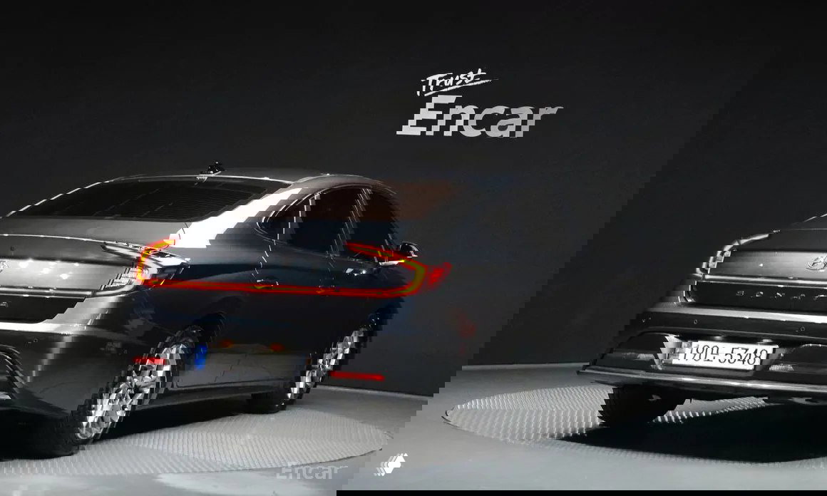 Задний вид Hyundai Sonata DN8 2021 в тёмном цвете: светодиодная задняя оптика, эмблема Sonata и вид на кузов в шоурумных условиях.