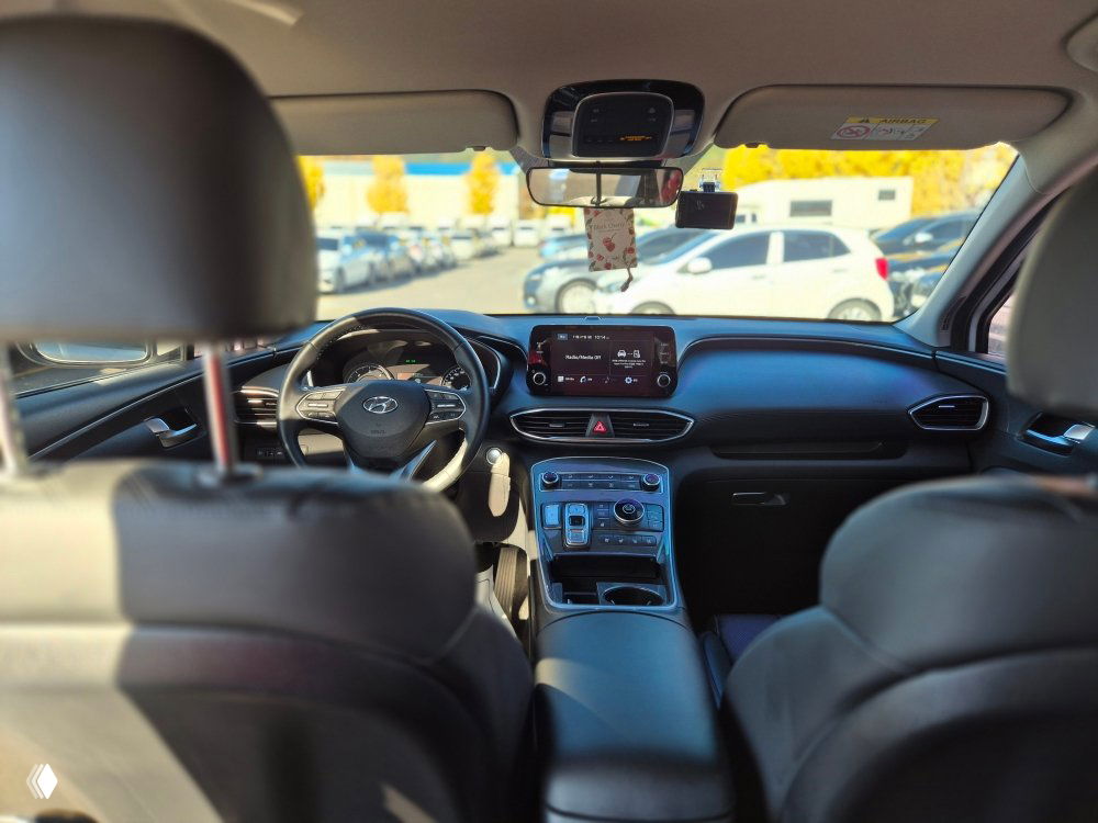 Интерьер Hyundai Santa Fe: вид сзади на панель приборов, мультимедиа-экран, руль и центральную консоль с селектором и подстаканниками.