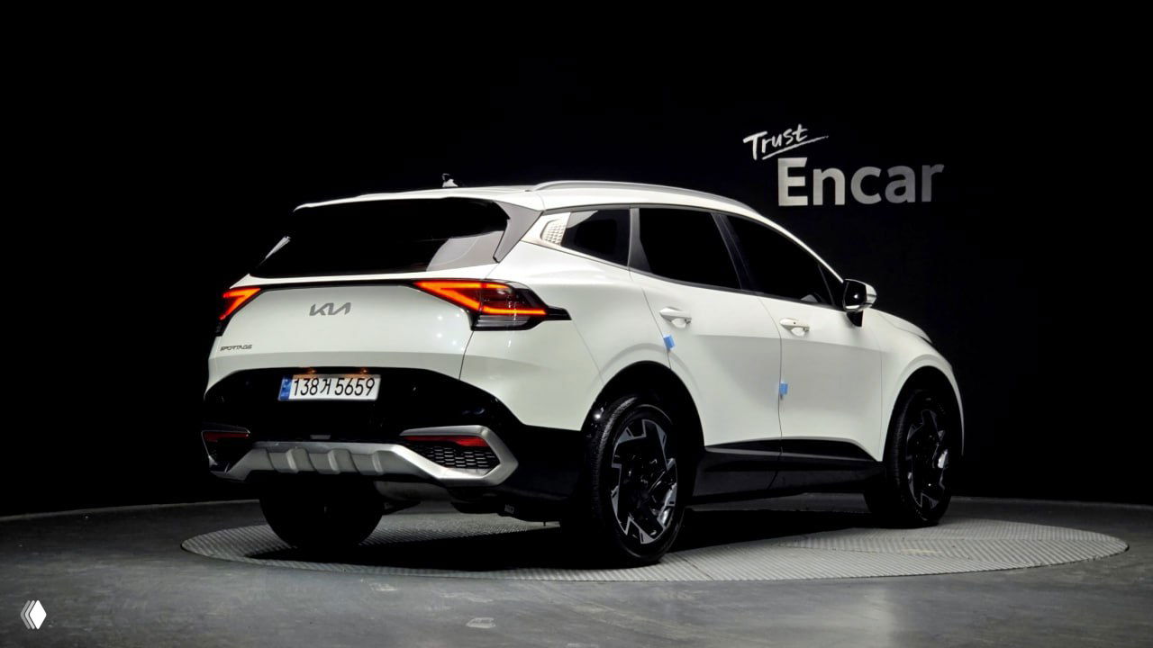 Фотография белого Kia Sportage 2023 — заднебоковой ракурс на студийной площадке, видны задние фонари, эмблема KIA и задняя часть кузова.