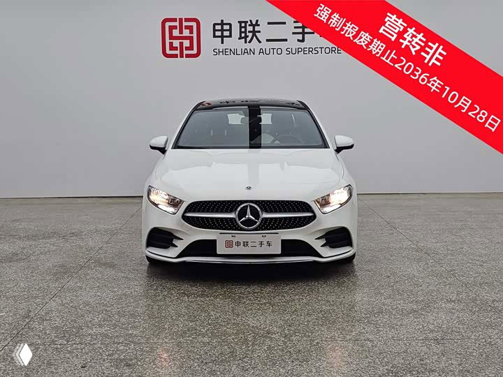 Фронтальный вид белого Mercedes‑Benz A 180 L с эмблемой на решётке и номерной табличкой дилера, фон студийный.