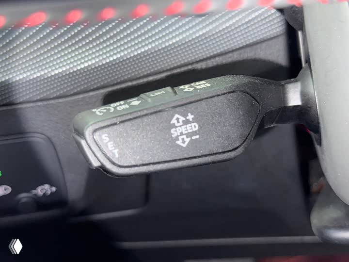 Крупный план рычага круиз‑контроля с маркировкой '+/- SPEED' внутри салона Audi Q2L, показаны элементы управления водителя.