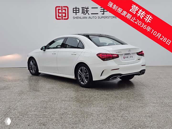 Задне‑боковой вид белого Mercedes‑Benz A 180 L в шоуруме, видна задняя оптика и двойной выпуск, пол и логотип дилера на стене.