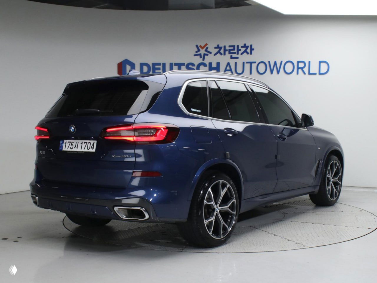 Задний вид BMW X5 в шоуруме: три четверти сзади, видно хромированные патрубки выхлопа, стильные задние фонари и легкосплавные диски.