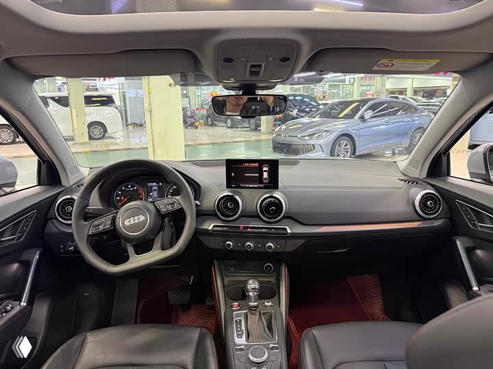 Вид салона Audi Q2L: панель приборов, рулевое колесо, центральный дисплей и центральная консоль в контексте выставочного зала.