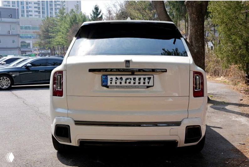 Белый Rolls‑Royce Cullinan, вид сзади на стоянке в Корее; заметны задние фонари, бампер и общий городской фон.