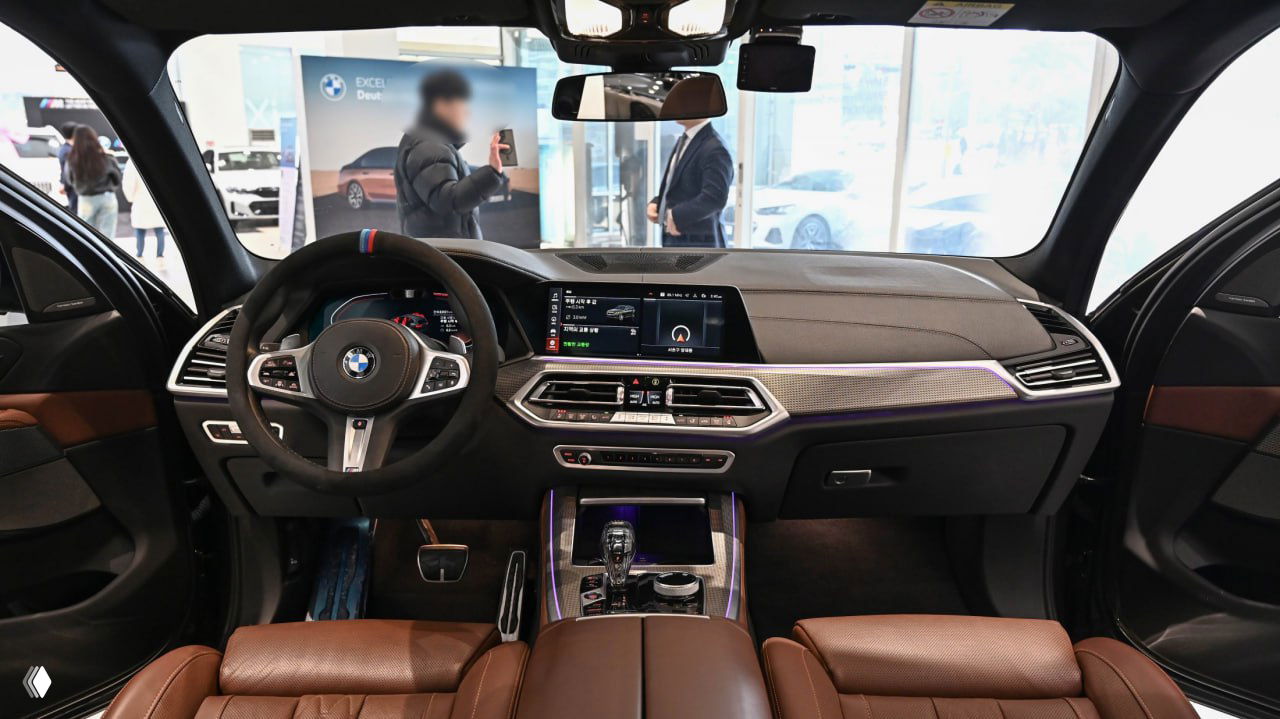 Интерьер BMW X5 G05: вид на рулевое колесо, центральную панель с дисплеем и коричневую кожаную отделку передних сидений в шоуруме.
