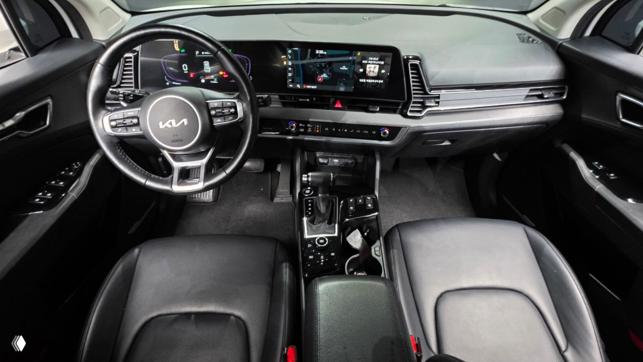 Фотография салона Kia Sportage 2023 — панорамный вид передней панели, руль с логотипом KIA, центральная консоль, рычаг переключения передач и передние кресла.