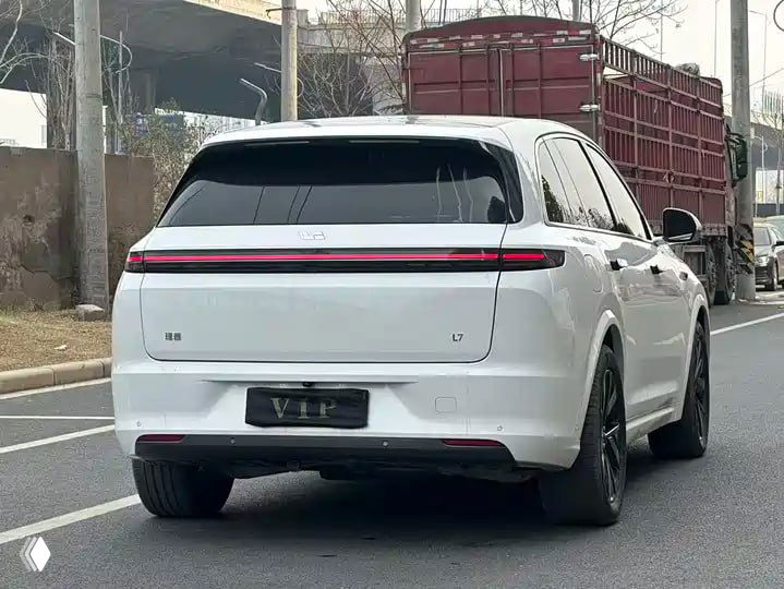 Вид сзади на белый Li Auto L7: светодиодная световая полоса на багажнике, номерной знак 'VIP', автомобиль на городской дороге при транспортировке.