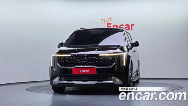 Чёрный Kia Carnival HEV 7 Noblesse 2025 в студийном освещении, вид спереди-центр с фирменной решёткой и эмблемой Kia.