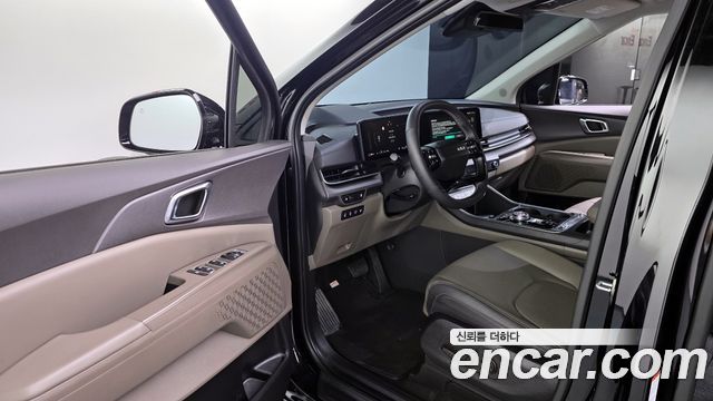 Салон Kia Carnival HEV 7 Noblesse 2025: передняя панель, руль, центральная консоль и дверь водителя, светло-бежевые вставки отделки.