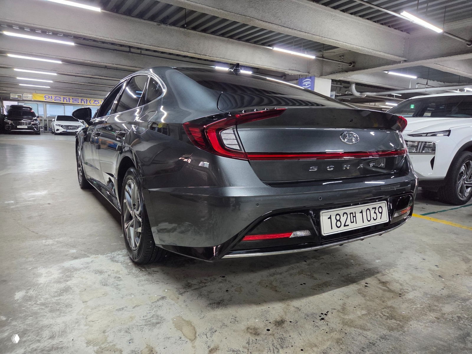Вид сзади серого Hyundai Sonata 2021 в крытой парковке: форма задних фонарей, линия багажника и корейский регистрационный знак видны на фото.
