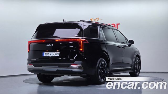 Задний ракурс Kia Carnival HEV 2025 на поворотном стенде Encar, видно светящуюся заднюю секцию и номерной знак.