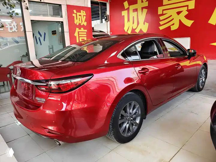 Вид сзади на красную Mazda Atenza 2021 в автосалоне, задняя часть автомобиля, багажник и задние фары на фоне стенда дилера.