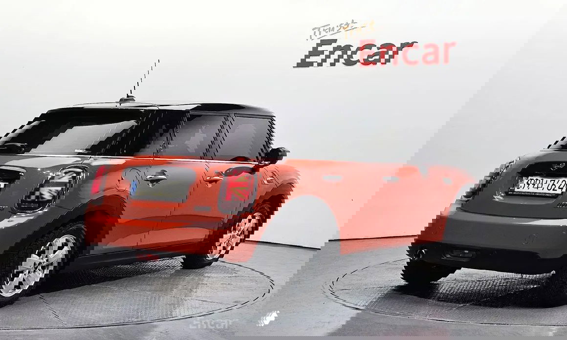 Задний ракурс оранжевого Mini Cooper 5‑door 2021 на подиуме дилера Encar, видна задняя оптика, номер и оформленная площадка.