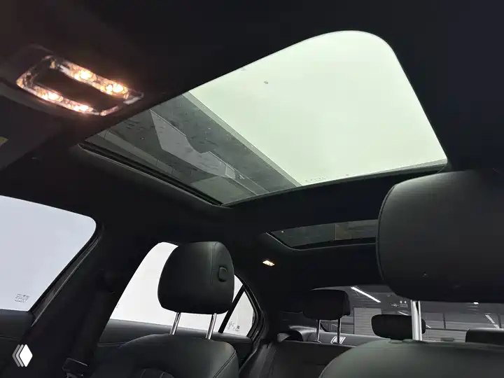 Панорамная крыша Mercedes‑Benz A‑Class A 180 L Sport Sedan 2022: обзор из задней части салона на стеклянный люк и передние сиденья, светлый фон.