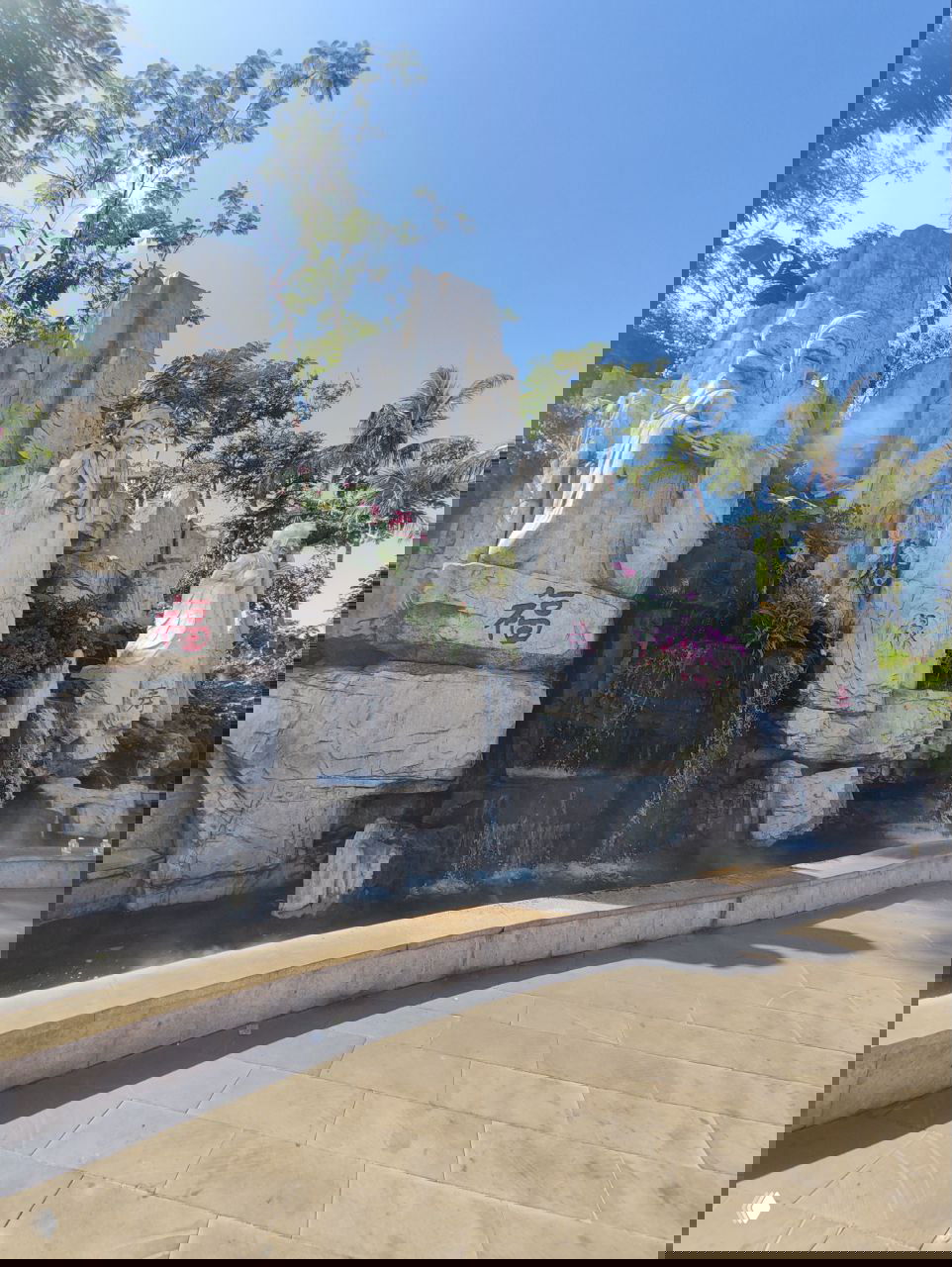 Пейзаж с каменными скульптурами и каскадом водопадов в оформленном саду; на камнях видны китайские символы и декоративная растительность.