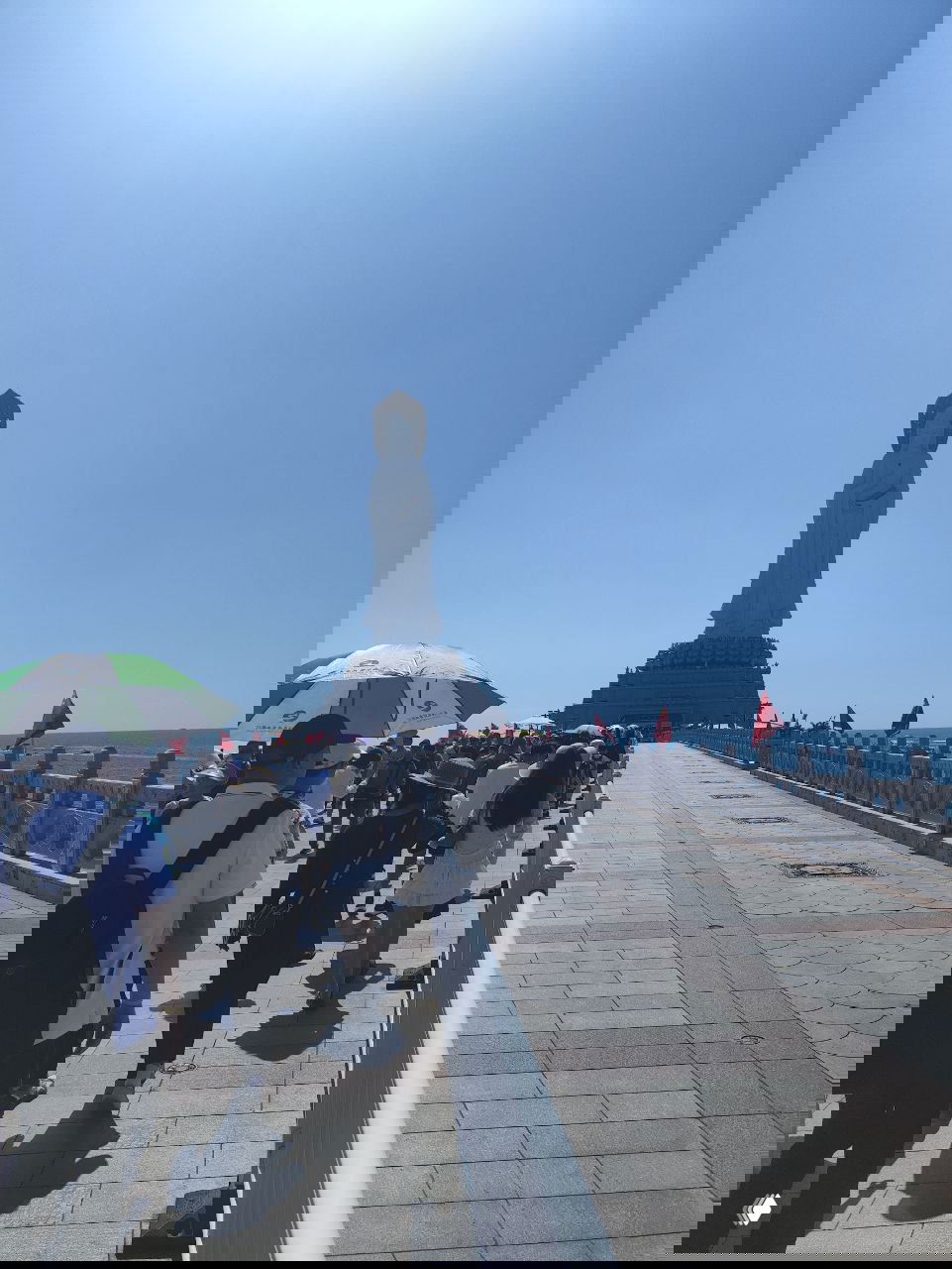 Панорамный вид с высоты на пирс и причал, ведущие к статуе Гуань Инь: пляж, прогулочные лодки и множество людей на мосту.