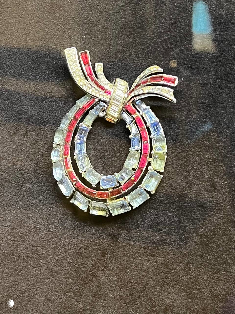 Крупный план винтажной броши в виде двойного овала с разноцветными прямоугольными кристаллами на бархатном тёмном фоне экспозиции.