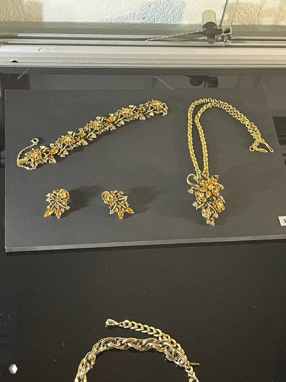 Набор винтажных украшений: браслет, серьги и ожерелье с янтарно-золотистыми кристаллами в витрине Музея янтаря на чёрном фоне.